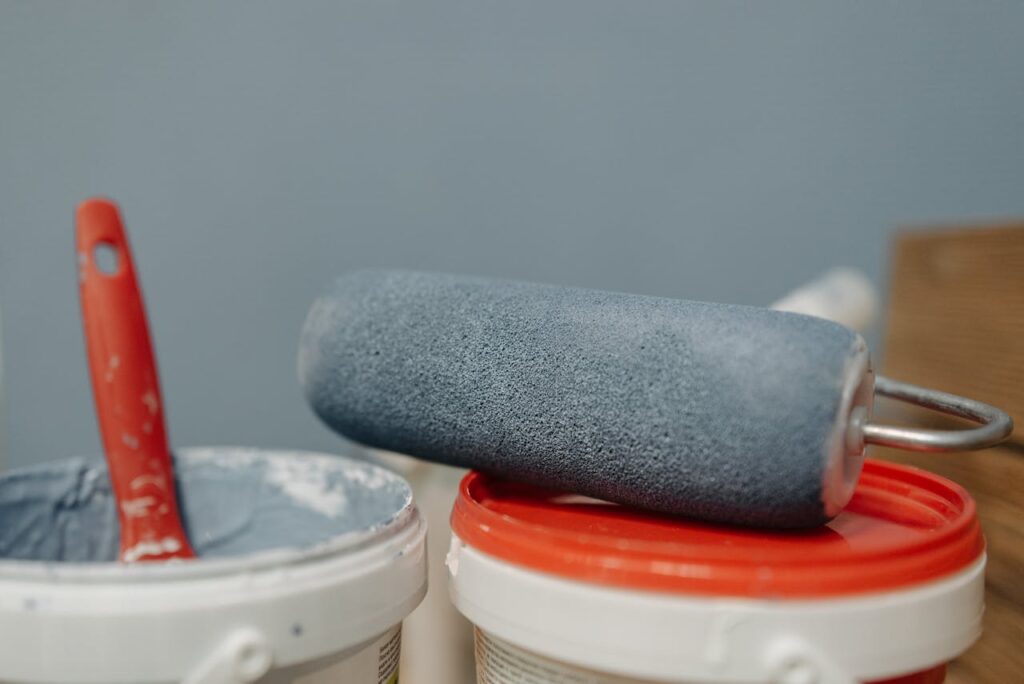A detailed look at a paint roller resting on paint buckets with a blue color scheme.